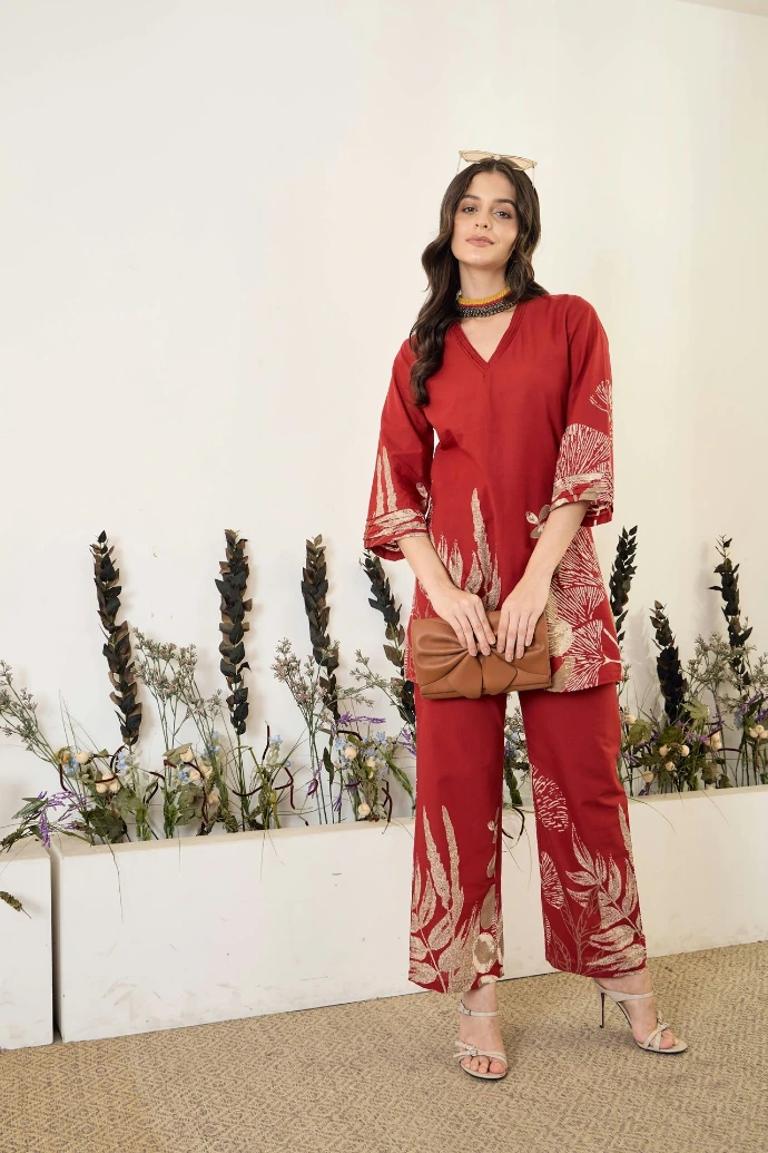 Woman in red patterned outfit holding a clutch bag.